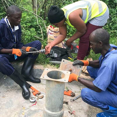 Drei Personen arbeiten an einer Handpumpe für Trinkwasser und tragen so zu einer zuverlässigen Wasserversorgung bei.