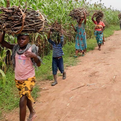 Kinder und Frauen tragen Brennholzbündel auf dem Kopf – symbolisch für den hohen Brennholzbedarf zum Abkochen von Trinkwasser.