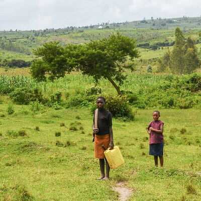 Zwei Mädchen in Ruanda mit Kanister auf einem Pfad durch grüne Hügellandschaft – unterwegs zum Wasserholen.