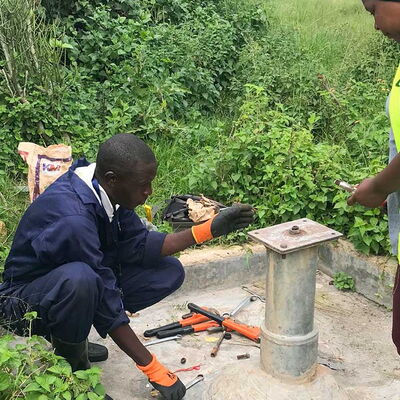 Zwei Personen installieren oder reparieren eine Handpumpe an einem Brunnen – für besseren Zugang zu sauberem Trinkwasser.