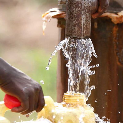 Wasser strömt aus einem Rohr in einen Kanister – Zugang zu sauberem Trinkwasser für Menschen in Ruanda.