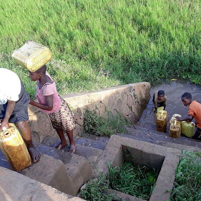 Personen in Ruanda, die Kanister vom Wasserloch eine steile Treppe hinauftragen – Sinnbild für Anstrengung beim täglichen Wasserholen.