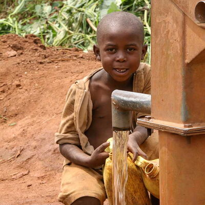 Junge sitzt an einer Handpumpe und füllt einen Kanister mit sauberem Wasser – er freut sich, weil er das Wasser bedenkenlos trinken kann.