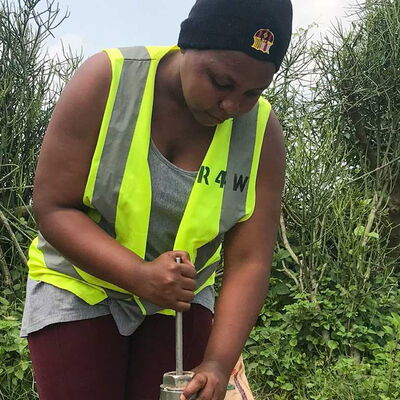 Frau in Warnweste arbeitet konzentriert an der Reparatur einer Handpumpe – Einsatz für sauberes Trinkwasser in Ruanda.