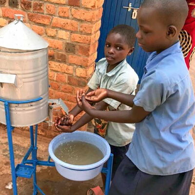 Zwei Kinder waschen sich aus einem Wasserspender die Hände – Symbol für Hygiene und sauberes Wasser.